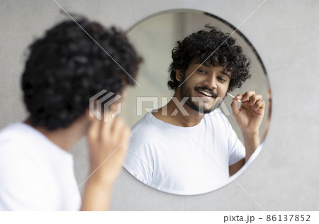 Daily hygiene routine. Indian man cleaning ears using cotton swab while doing morning beauty routine in bathroom Daily hygiene routine. Indian man cleaning ears using cotton swab while doing morning beauty routine in bathroom 86137852