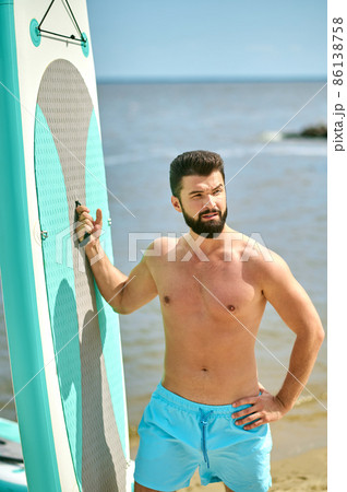 A well-built young man with a surfing board on a beach 86138758