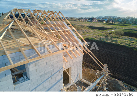 Aerial view of unfinished frame of private house with aerated lightweight concrete walls and wooden roof frame under construction. 86141560