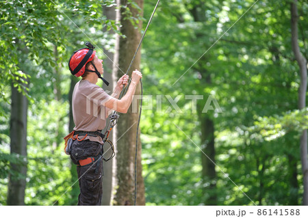 Man belays his partner climber with belaying device and rope. Climber's handsman holding equipment for rock mountaineering security. Man belays his partner climber with belaying device and rope. Climber's handsman holding equipment for rock mountaineering security. 86141588