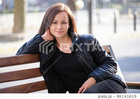 Young happy woman sitting relaxed on street bench on warm autunm day. Wellness and resting from everyday rush concept Young happy woman sitting relaxed on street bench on warm autunm day. Wellness and resting from everyday rush concept 86141619
