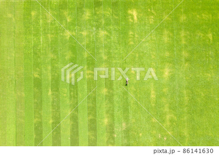 Aerial view of small figure of man worker trimming green grass with mowing mashine on football stadium field in summer. Aerial view of small figure of man worker trimming green grass with mowing mashine on football stadium field in summer. 86141630