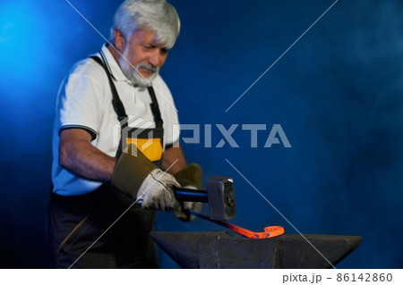 Skillful blacksmith forging molten steel on anvil  86142860