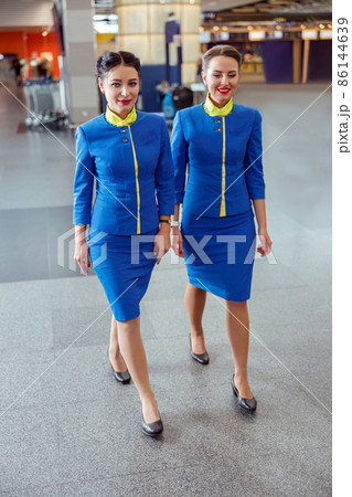Cheerful women stewardesses walking down airport terminal Cheerful women stewardesses walking down airport terminal 86144639