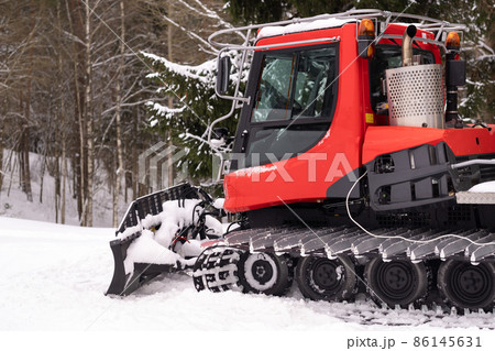 A snowplow on red tracks standing in winter in the forest near the barn A snowplow on red tracks standing in winter in the forest near the barn 86145631