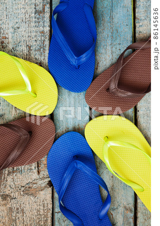 stack of several pairs of multi-colored rubber flip flops on a blue wooden background 86145636