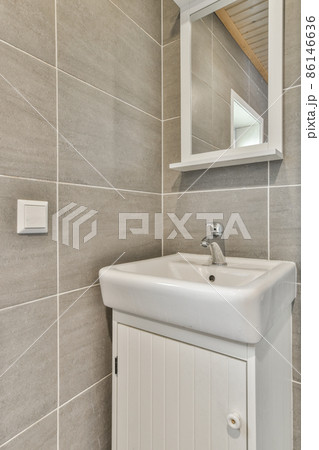 Whire ceramic sink and mirror on the wall in a modern bright bathroom with grey tiles Whire ceramic sink and mirror on the wall in a modern bright bathroom with grey tiles 86146636