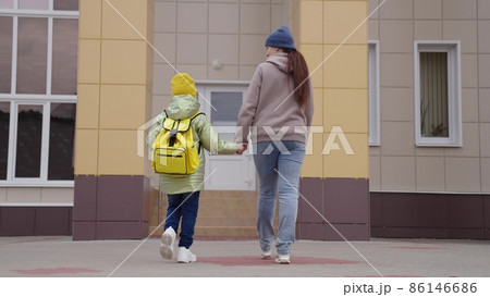 affectionate mother leads the child back to school, to teach first lessons of childhood, a school student goes hand in hand with mom, happy family, a cheerful boy son with mom go to school building 86146686