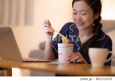 夜のリビング　パソコンを見ながらカップラーメンを食べる女性 86152030