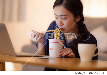 夜のリビング　パソコンを見ながらカップラーメンを食べる女性 86152031