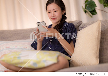 夜のリビング　ソファーに座りスマホを見ながら寛ぐ女性 86152054