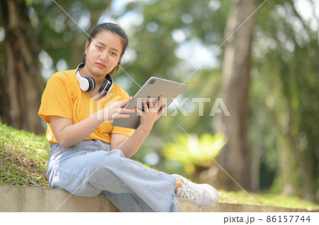Teenage girl wearing headphones on neck holding tablet looking at camera serious expression. Teenage girl wearing headphones on neck holding tablet looking at camera serious expression. 86157744