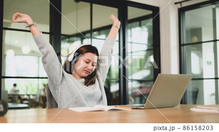 A teenage girl wears headphones with her arms up to relax during an online class. A teenage girl wears headphones with her arms up to relax during an online class. 86158203
