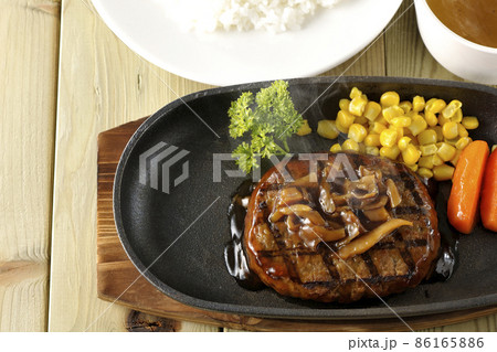 鉄板の上のパセリ、グラッセ、コーン、きのこソースの熱々和風ハンバーグステーキとコンソメスープとライス 鉄板の上のパセリ、グラッセ、コーン、きのこソースの熱々和風ハンバーグステーキとコンソメスープとライス 86165886