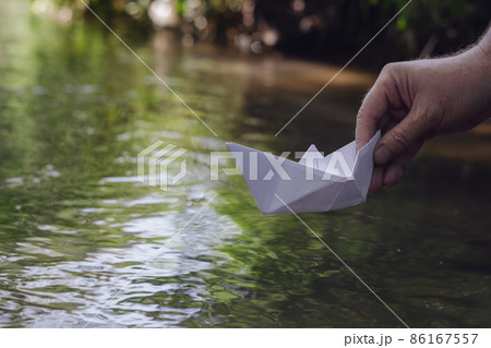 A hand lowers a white paper boat on the water. 86167557