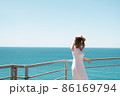 Young woman in white dress and hat stands by the sea. 86169794