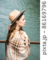 Beautiful woman in a white long dress and hat is standing by the water and smiling. Travel concept. 86169796