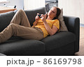 Young woman lying on the couch and using smartphone for speak with friends and relatives. 86169798