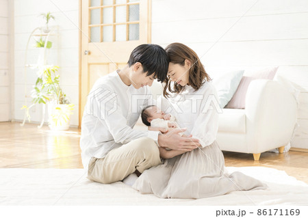 リビングに座って微笑む若いママとパパと赤ちゃん3人のポートレート リビングに座って微笑む若いママとパパと赤ちゃん3人のポートレート 86171169