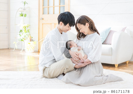 リビングに座って微笑む若いママとパパと赤ちゃん3人のポートレート 86171178