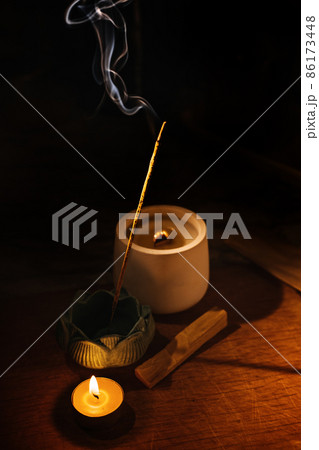 Incense aroma sticks smoldering on table lotus holder and candle in darkness. Zen, meditation, mental health comfort zone Incense aroma sticks smoldering on table lotus holder and candle in darkness. Zen, meditation, mental health comfort zone 86173448