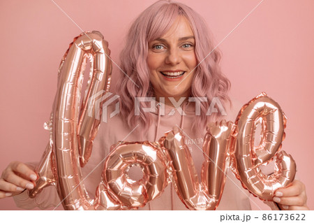 Valentine's Day banner with pretty young 20s woman celebration having fun holding foil love word balloons over pink background. Mother's day, Birthday. 86173622