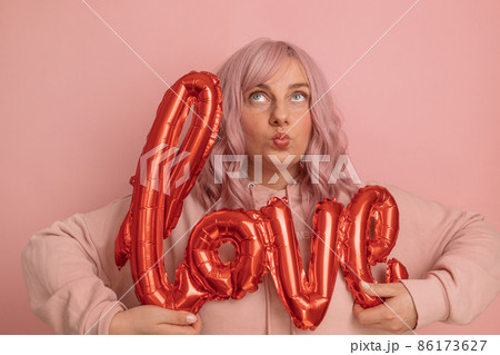 Valentine's Day banner with pretty young 20s woman having fun holding red foil love word balloons over pink background. Mother's day, Birthday. 86173627