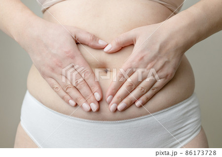 Closeup cropped of unrecognizable plus size woman in underwear holding hands on abdominal area forming heart shape around navel Closeup cropped of unrecognizable plus size woman in underwear holding hands on abdominal area forming heart shape around navel 86173728