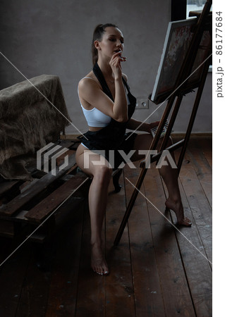 Alluring woman in apron drawing picture at easel Alluring woman in apron drawing picture at easel 86177684