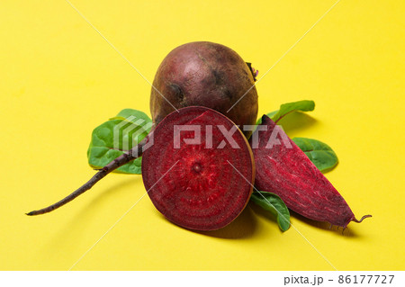 Ripe red beet with leaves on yellow background Ripe red beet with leaves on yellow background 86177727