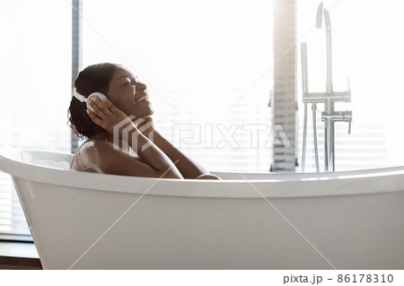 Relaxed african american woman taking bath and listening music Relaxed african american woman taking bath and listening music 86178310