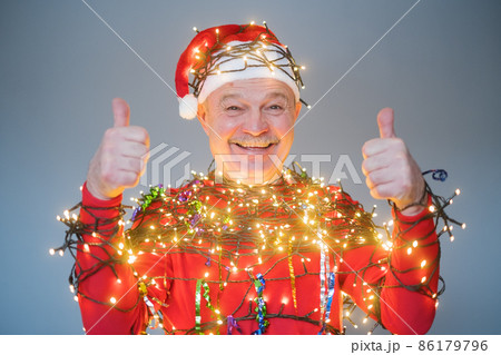 Senior man in red christmas hat wrapped in garland. Senior man in red christmas hat wrapped in garland. 86179796