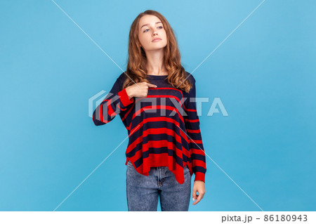 Self confident egoistic woman wearing sweater pointing on herself with arrogance and satisfaction, proud of herself, bragging with achievements. Indoor studio shot isolated on blue background. 86180943