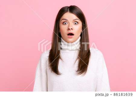 Shocked scared girl looking at camera with opened mouth and big eyes, sees something astonishing, wearing white casual style sweater. Indoor studio shot isolated on pink background. Shocked scared girl looking at camera with opened mouth and big eyes, sees something astonishing, wearing white casual style sweater. Indoor studio shot isolated on pink background. 86181639