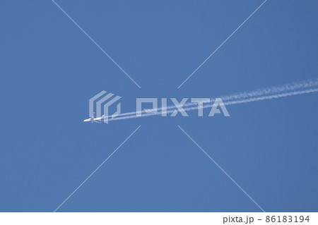 Distant passenger jet plane flying on high altitude on clear blue sky leaving white smoke trace of contrail behind. Air transportation concept 86183194
