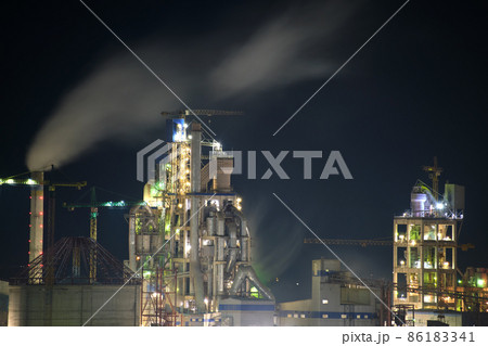 Illuminated cement plant with high factory structure and tower cranes at industrial production area at night. Manufacture and global industry concept 86183341