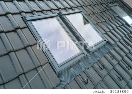 Closeup of attic window on house roof top covered with ceramic shingles. Tiled covering of building Closeup of attic window on house roof top covered with ceramic shingles. Tiled covering of building 86183396