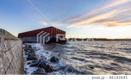 Barge container ship collided on a rocky coast during wind storm. Sunset Sky. Barge container ship collided on a rocky coast during wind storm. Sunset Sky. 86183685