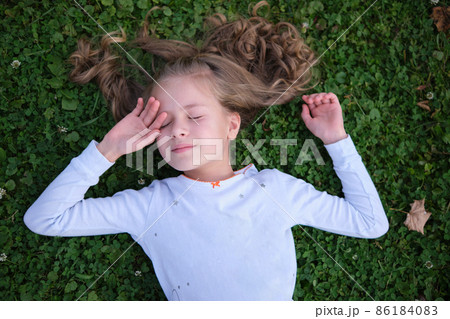 Portrait of pretty child girl outdoors lying down on grass lawn 86184083