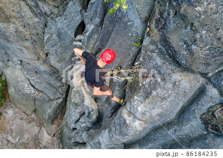 Strong male climber climbing steep wall of rocky mountain. Sportsman overcoming difficult route. Engaging in extreme sports hobby concept. 86184235