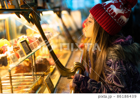 A child in winter clothes and a Christmas red hat chooses sweets in a shop window to buy. The concept of New Year holidays, discounts, shopping. 86186439