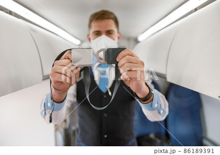 Male flight attendant in safety face mask holding seatbelt 86189391