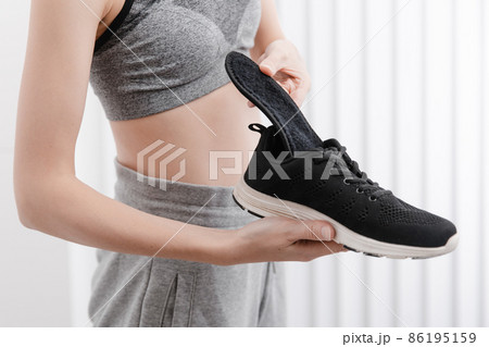 Woman putting orthopedic insole into shoe at home. Sports girl fitting orthopedic insole indoors, close up. Foot care banner. Flat Feet Correction. Treatment and prevention of foot diseases. 86195159