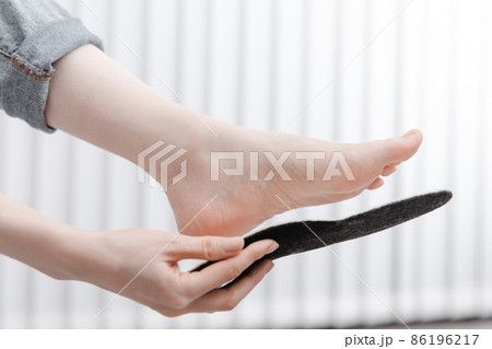 Woman fitting orthopedic insole indoors, close up. Girl holding an insole next to foot at home. Orthopedic insoles. Foot care banner. Flat Feet Correction. Treatment and prevention of foot diseases. 86196217