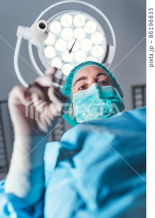 From below woman surgeon in medical uniform using professional tools while standing under bright 86196835