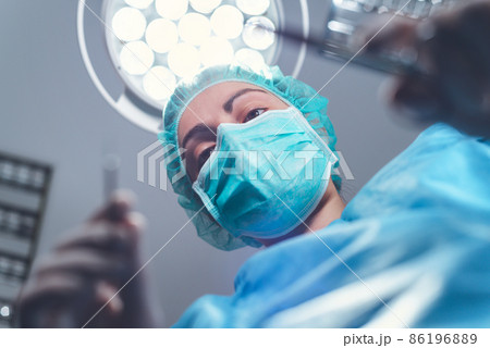 From below woman surgeon in medical uniform using professional tools while standing under bright 86196889