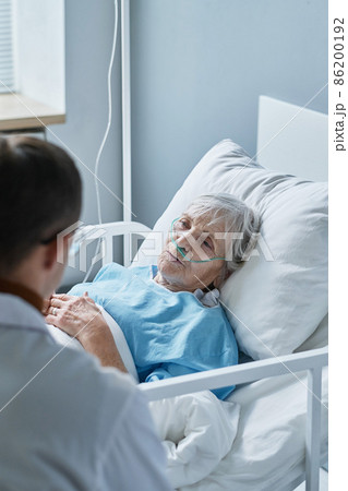 Sick senior woman lying on hospital bed and talking to her doctor about her health during pandemic at hospital 86200192