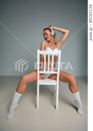 Banner of young happy girl in white swimsuit listening to music in white chair, wearing wireless headhones, isolated on gray background with copy space in studio Banner of young happy girl in white swimsuit listening to music in white chair, wearing wireless headhones, isolated on gray background with copy space in studio 86202138