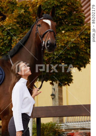 Female horseman going with her brown horse outdoor. Concept of animal care. Rural rest and leisure. Idea of green tourism. Young european woman wearing uniform 86202179