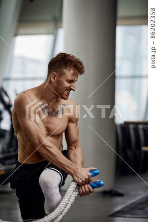 Front view of Attractive young fit and toned sportswoman working out with battle ropes. Motion blur 86202358